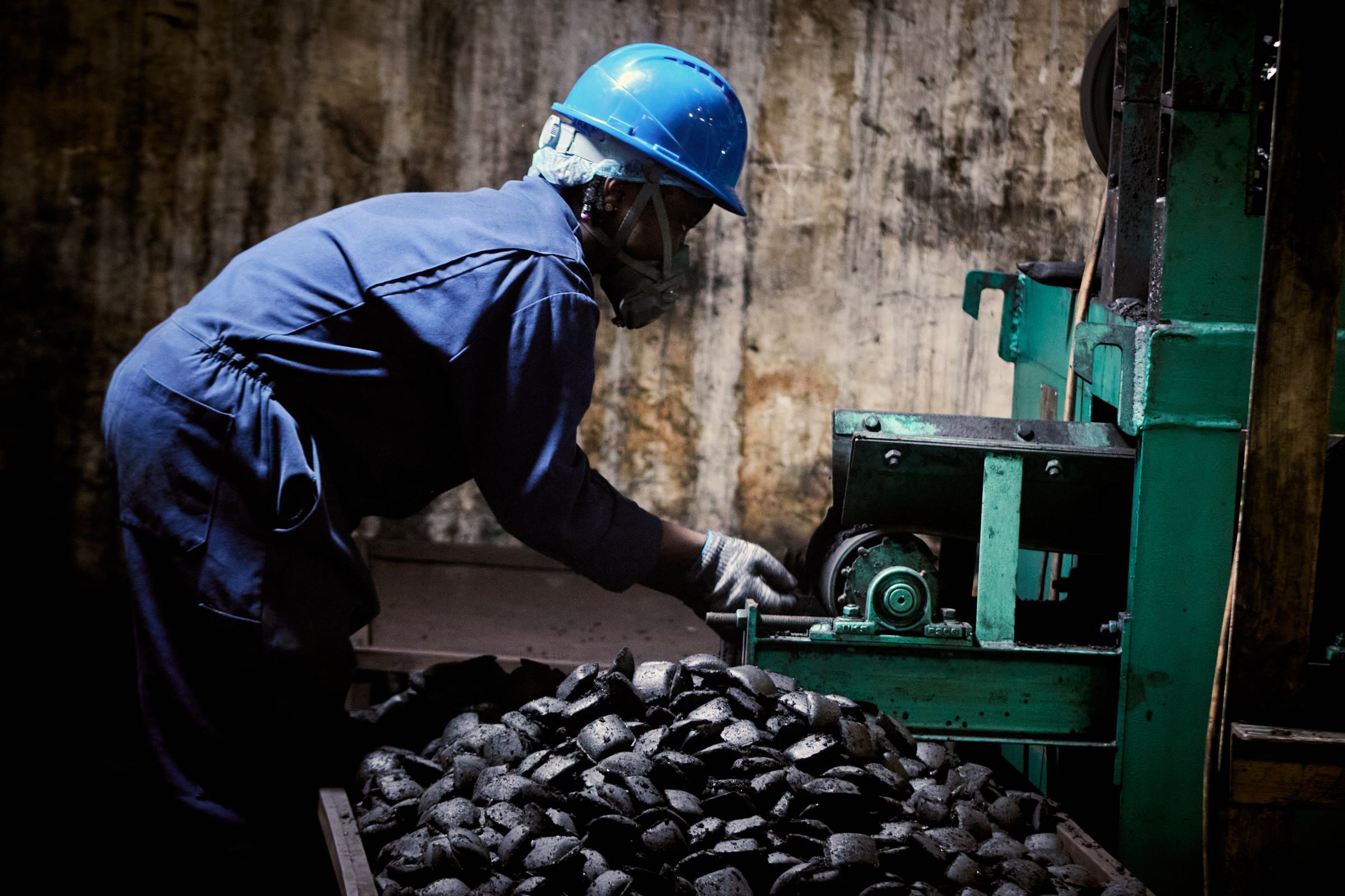 A worker at the briquette press, freshly pressed char-briquettes filling the tray